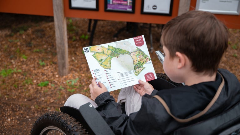 Young visitor who is a wheelchair user views a map of Oxburgh Estate